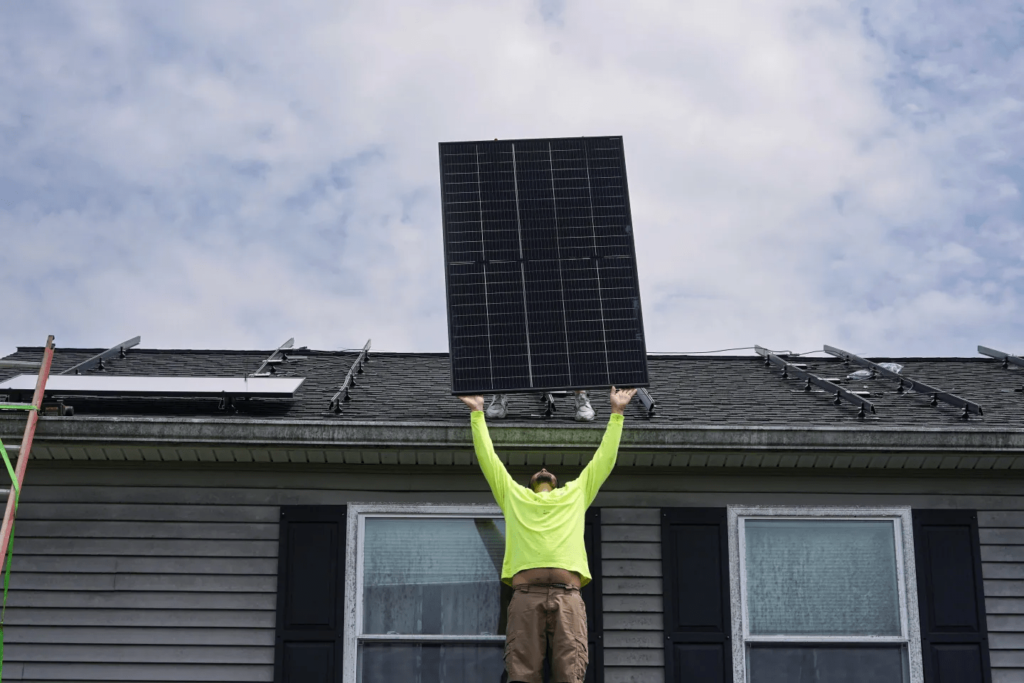 Nicholas Hartnett, owner of Pure Power Solar, lifts a solar panel to the roof of a home in Frankfort, Ky., on July 17, 2023.